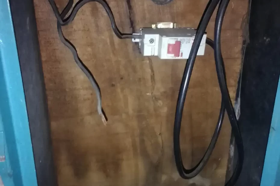 Falhas elétricas na fiação com disjuntor mal fixado, fios expostos e instalação sobre madeira, aumentando o risco de curto-circuito e incêndio