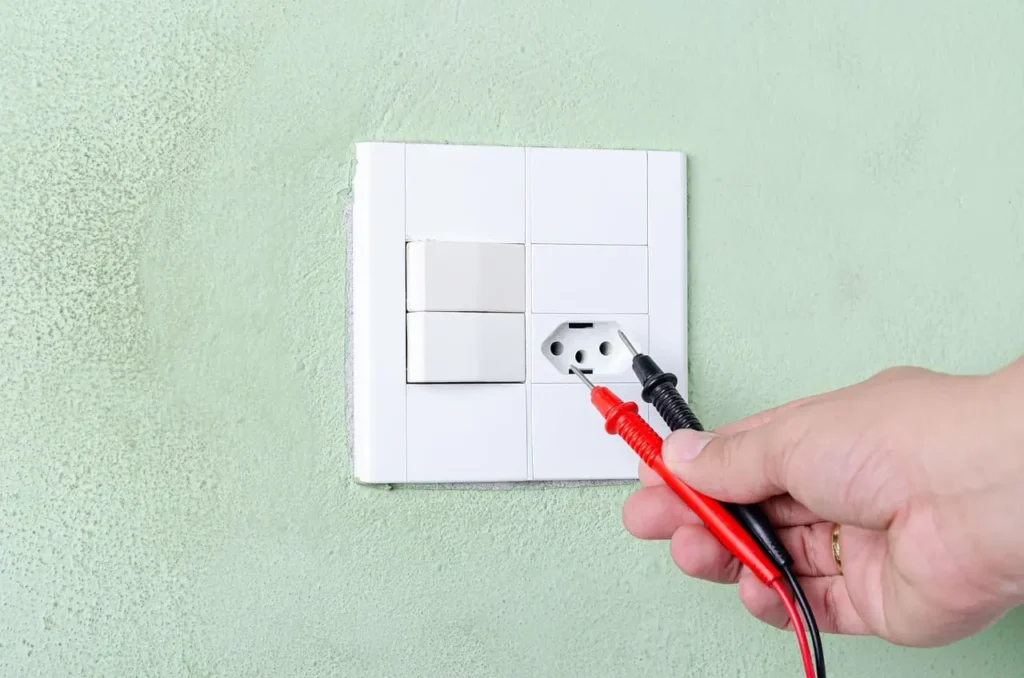 Técnico medindo tensão em tomada com voltímetro para identificar energia fraca na residência e possíveis causas